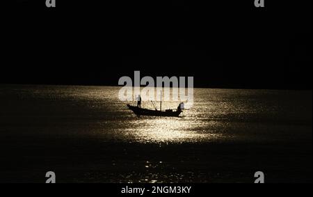 Bateau de pêche pris dans le coucher du soleil silhoueté contre l'eau et les montagnes en arrière-plan dans la province de Chumphon en Thaïlande Banque D'Images