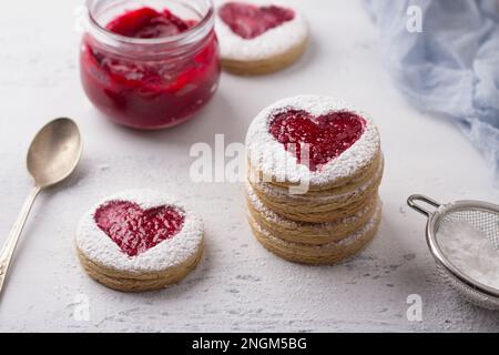 Biscuit épicé à la maison avec cœur rouge avec confiture sur plaque blanche et une tasse de café sur fond texturé gris, pour la Saint-Valentin Banque D'Images
