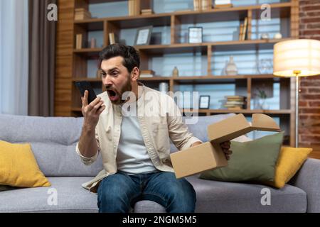 Un homme furieux a triché à la maison avec le téléphone et le colis reçu, arguant par téléphone en parlant au service d'assistance à la clientèle de la boutique en ligne, la livraison du produit a échoué. Banque D'Images