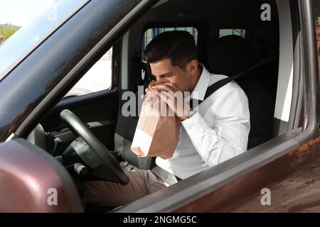 Homme avec sac en papier souffrant de nausées dans la voiture Banque D'Images