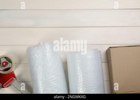 Rouleaux d'emballage à bulles, boîte en carton et distributeur de ruban adhésif sur fond en bois blanc, pose à plat. Espace pour le texte Banque D'Images