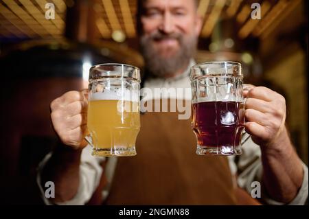 Brasseur senior satisfait posant pour caméra avec de la bière pâle et de la bière foncée pinte Banque D'Images