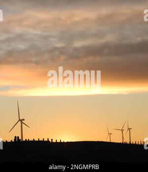 Le soleil se plonge sous l'horizon et produit une lueur dorée avec des éoliennes et une clôture en silhouette en premier plan inférieur Banque D'Images