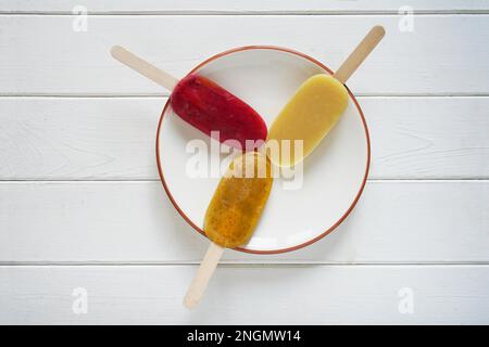 Vue de dessus de trois différentes sucettes glacées smoothie aux fruits ou glace pop sur une plaque sur fond de bois blanc Banque D'Images