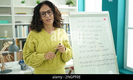 Femme hispanique d'âge moyen enseignant expliquant l'exercice de mathématiques à l'université de bibliothèque Banque D'Images