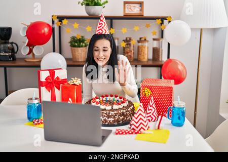 Femme hispanique célébrant son anniversaire avec un grand gâteau au chocolat faisant un appel vidéo qui a l'air positif et heureux debout et souriant avec un sourire confiant SH Banque D'Images
