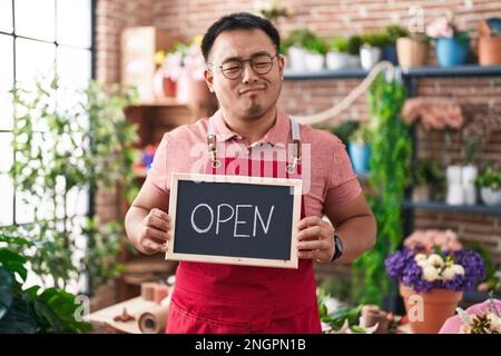 Jeune homme chinois travaillant chez un fleuriste tenant un panneau ouvert souriant regardant sur le côté et regardant loin de penser. Banque D'Images