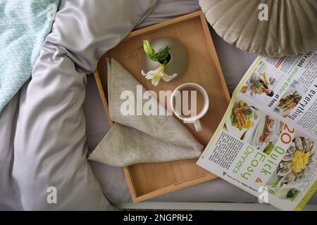 Plateau avec tasse de café, fleur et magazine sur linge de lit frais, vue du dessus Banque D'Images