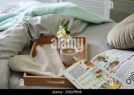 Tasse de café, fleur et magazine sur le lit avec linge frais à l'intérieur Banque D'Images