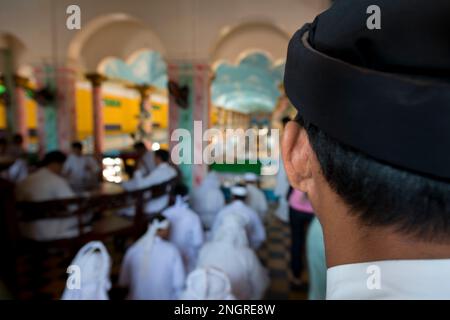 Vue de derrière le disciple de Nake Caodaist avec chapeau près des musiciens jouant des instruments pendant la cérémonie, Temple de Cao Dai, Tay Ninh, près de HCMC, Vietnam Banque D'Images