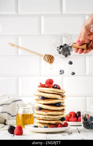 pile de crêpes avec levitation de baies. À proximité, il y a un pot de miel, des bols avec des bleuets et des framboises, une cuillère à miel levante Banque D'Images