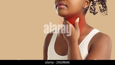 Inconnue jeune femme à la peau foncée tenant sa gorge sur fond beige. Bannière. Banque D'Images