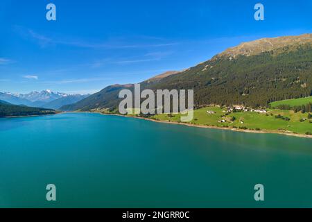 Vue aérienne du lac (Reschensee). Grand réservoir entouré de montagnes à midi ensoleillé. Espace de loisirs pour les touristes et les sportifs. Ferme biologique sur t Banque D'Images