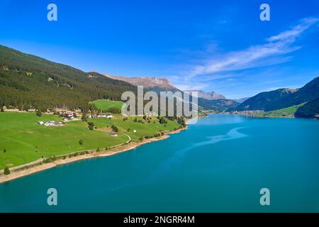 Vue aérienne du lac (Reschensee). Grand réservoir entouré de montagnes à midi ensoleillé. Espace de loisirs pour les touristes et les sportifs. Ferme biologique sur t Banque D'Images