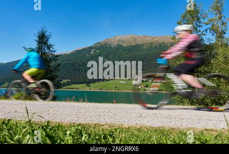 2 cyclistes en mouvement. Adultes faisant du sport à vélo l'après-midi ensoleillé d'été, au lac dans les montagnes. Italie, Vinschgau, Lac Resia (Reschens Banque D'Images