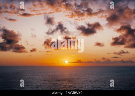 L'étendue infinie de l'horizon océanique au coucher du soleil, comme les nuages roses, orange et pourpres remplissent le ciel. Banque D'Images