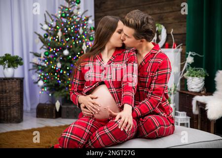 Une femme enceinte et un homme baiser sur les lèvres tout en étant assis sur un canapé Banque D'Images