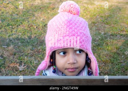 mignon sourire afro-américaine bébé fille en tenue blanche à l'extérieur au coucher du soleil portant un bonnet en tricot beanie rose avec rabats d'oreilles Banque D'Images