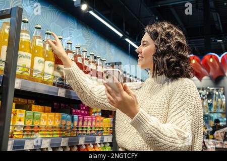 Une femme achète du jus de la liste d'épicerie téléphonique de l'épicerie Banque D'Images