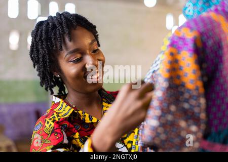 Souriant dressmaker ouest-africain avec des cheveux locs mesure une partie d'une robe dans son studio de design Banque D'Images