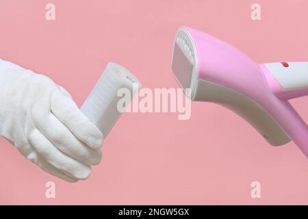 Homme des gants tenant un défroisseur de vêtements démonté avec un réservoir d'eau en plastique. fond rose. Banque D'Images