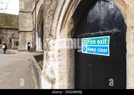 Foyer peu profond d'un panneau de sortie de feu vu attaché à une porte médiévale en bois située à la base d'une église. Une visite de l'église peut être vue. Banque D'Images