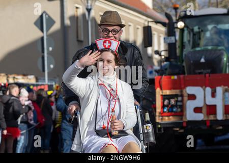 Radeburg, Allemagne. 19th févr. 2023. Un homme pousse une femme dans un fauteuil roulant de l'autre côté de la rue pendant le défilé de carnaval dans la petite ville saxonne de Radeburg. C'est l'un des plus grands de ce genre en Saxe. Credit: Daniel Schäfer/dpa/Alay Live News Banque D'Images