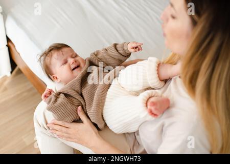 Malade nouveau-né de 4-5 mois avec douleur colique sur les mains de la mère dans la chambre vue du dessus. Femme essayez de calmer son bébé pleurant dans le lit. Soins de santé. Maternité. Banque D'Images