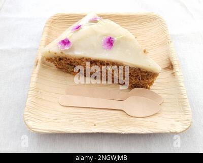 Une tranche de gâteau de carotte fait maison à base d'ingrédients biologiques pour végétariens et végétaliens, sur une assiette et des cuillères en bois, des ustensiles recyclables. Banque D'Images