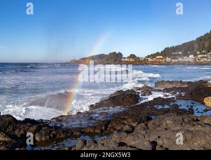 La ville de Yachats dans l'Oregon en arrière-plan, avec un arc-en-ciel au premier plan, formé par la lumière du soleil réfractaire dans la brume d'un cornet Banque D'Images