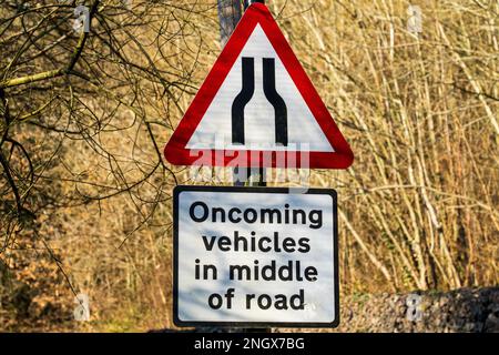 Le panneau de signalisation du Royaume-Uni indiquant que la route se rétrécit devant vous et que les véhicules arrivant en face seront au milieu de la route sur un triangle d'avertissement rouge et blanc Banque D'Images