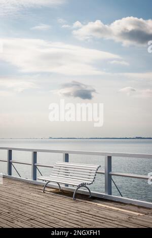 Banc blanc vide sur la jetée au bord de la mer Baltique. Paysage tranquille avec nuages sur le ciel Banque D'Images