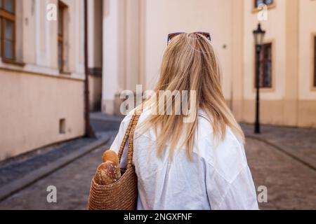 Une femme avec sac en paille réutilisable marche dans la rue dans la vieille ville européenne. Style de vie durable et vie urbaine Banque D'Images