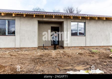 Une résidente se tient devant sa maison rénovée qui a été bombardée il y a un an sur la rue Vokzalna. La femme est restée à Bucha pendant la bataille de mars 2022, elle se cachait dans des abris scolaires locaux. Alors que l'invasion à grande échelle de l'Ukraine par les forces russes approche son premier anniversaire, les résidents de Bucha collectent des fonds pour reconstruire leurs maisons. La plupart des habitants de la rue Vokzalna, l'une des rues les plus détruites lors de la lutte pour défendre Kiev en mars 2022, ont maintenant la chance de reconstruire ou de rénover leurs maisons. Il y a d'autres parties de Bucha, ainsi que le voisin Irpin qui a encore wa Banque D'Images