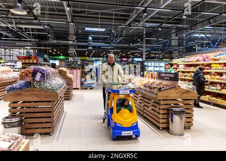 Bucha, Oblast de Kiev, Ukraine. 18th févr. 2023. Un acheteur marche avec un enfant dans un supermarché qui a été directement touché par l'occupation russe l'année dernière. Alors que l'invasion à grande échelle de l'Ukraine par les forces russes approche son premier anniversaire, les résidents de Bucha collectent des fonds pour reconstruire leurs maisons. La plupart des habitants de la rue Vokzalna, l'une des rues les plus détruites lors de la lutte pour défendre Kiev en mars 2022, ont maintenant la chance de reconstruire ou de rénover leurs maisons. Il y a d'autres parties de Bucha, ainsi que le voisin Irpin qui attendent encore des projets de rénovation. (Image de crédit : Banque D'Images