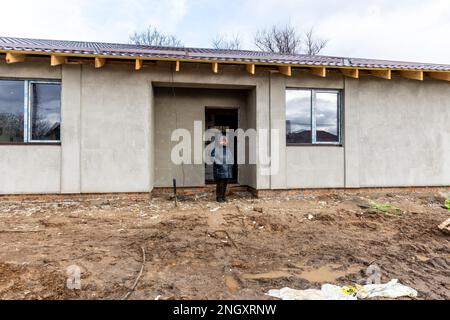 Bucha, Oblast de Kiev, Ukraine. 18th févr. 2023. Une résidente se tient devant sa maison rénovée qui a été bombardée il y a un an sur la rue Vokzalna. La femme est restée à Bucha pendant la bataille de mars 2022, elle se cachait dans des abris scolaires locaux. Alors que l'invasion à grande échelle de l'Ukraine par les forces russes approche son premier anniversaire, les résidents de Bucha collectent des fonds pour reconstruire leurs maisons. La plupart des habitants de la rue Vokzalna, l'une des rues les plus détruites lors de la lutte pour défendre Kiev en mars 2022, ont maintenant la chance de reconstruire ou de rénover leurs maisons. Il y a d'autres parties de B Banque D'Images