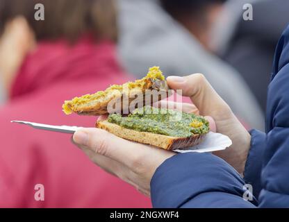 Un visiteur du marché agricole de Prague tient un plateau de papier avec un en-cas, des toasts avec du pesto aux herbes. Banque D'Images