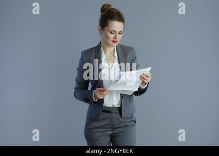 pensive moderne 40 ans femme travailleur en costume gris avec document sur fond gris. Banque D'Images