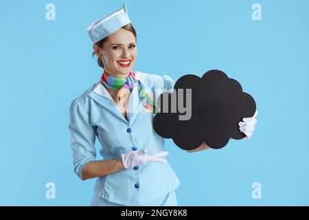 bonne femme élégante hôtesse de l'air isolée sur fond bleu uniforme bleu montrant un tableau blanc en forme de nuage. Banque D'Images