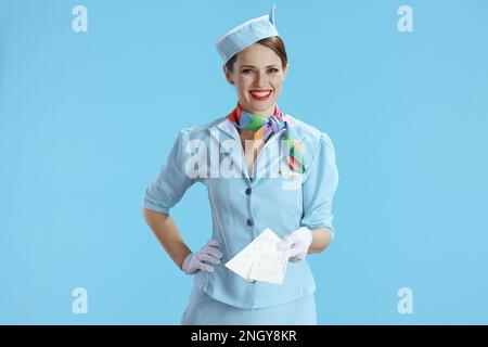 une femme élégante et heureuse navigante sur fond bleu en uniforme bleu avec billets d'avion. Banque D'Images