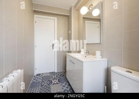 Salle de bains avec mobilier laqué blanc, comptoir en résine blanche, carrelage hydraulique et miroir carré sans cadre au mur Banque D'Images