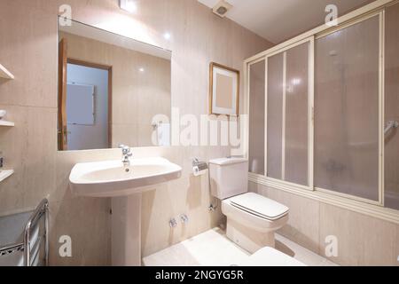 Salle de bains avec lavabo en porcelaine sur pied assorti, cabine de douche avec baignoire, grand miroir sans cadre et carrelage clair Banque D'Images