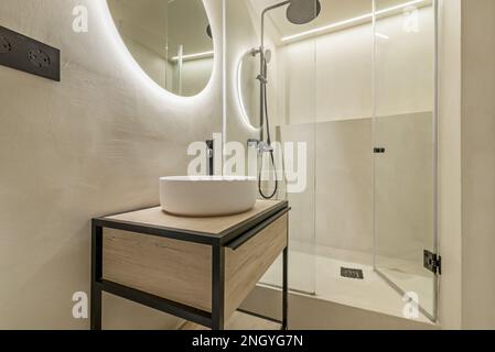 Salle de bains de style industriel meuble lavabo en bois et fer avec miroir circulaire avec cabine de douche en verre avec porte et robinets noirs Banque D'Images