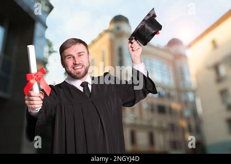 Joyeux étudiant avec un chapeau de diplôme et un diplôme en plein air Banque D'Images