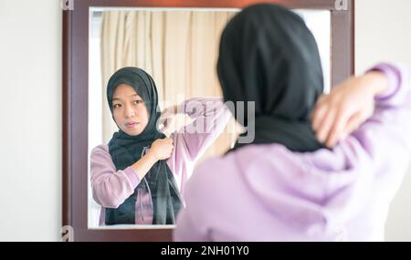 Réflexion sur un miroir mural d'une femme musulmane portant et ajustant son foulard. Banque D'Images