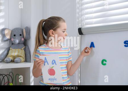 Petite fille montrant la lettre A sur le tableau blanc en classe. Cours d'anglais Banque D'Images