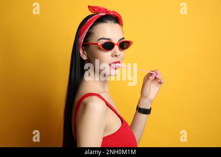 Jeune femme à la mode dans une tenue à épingler mâchant du bubblegum sur fond jaune Banque D'Images