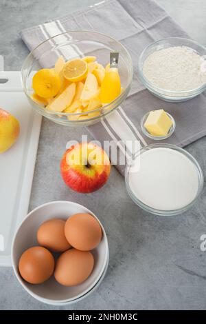 Moule à pâtisserie avec des tranches de pomme, des œufs, du sucre et de la farine dans des bols gros plan sur une table de cuisine, bannière verticale. Recette de gâteau aux pommes, processus de préparation Banque D'Images