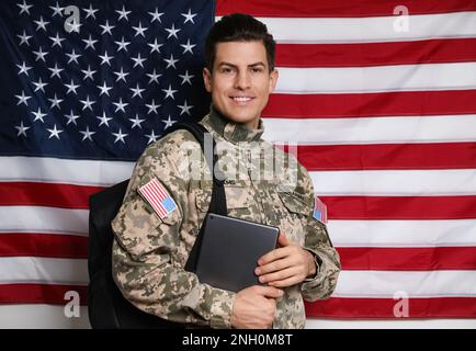 Cadet avec sac à dos et tablette contre le drapeau américain. Éducation militaire Banque D'Images