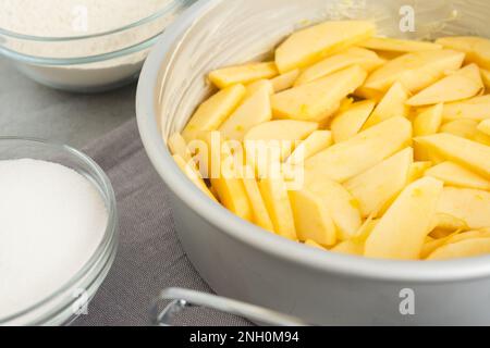 Moule à pâtisserie avec des tranches de pomme, du sucre et de la farine dans des bols en gros plan sur une table de cuisine. Recette de gâteau aux pommes, processus de préparation Banque D'Images